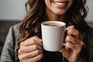 A lady smiling with stain free teeth and holding a cup of mushroom coffee